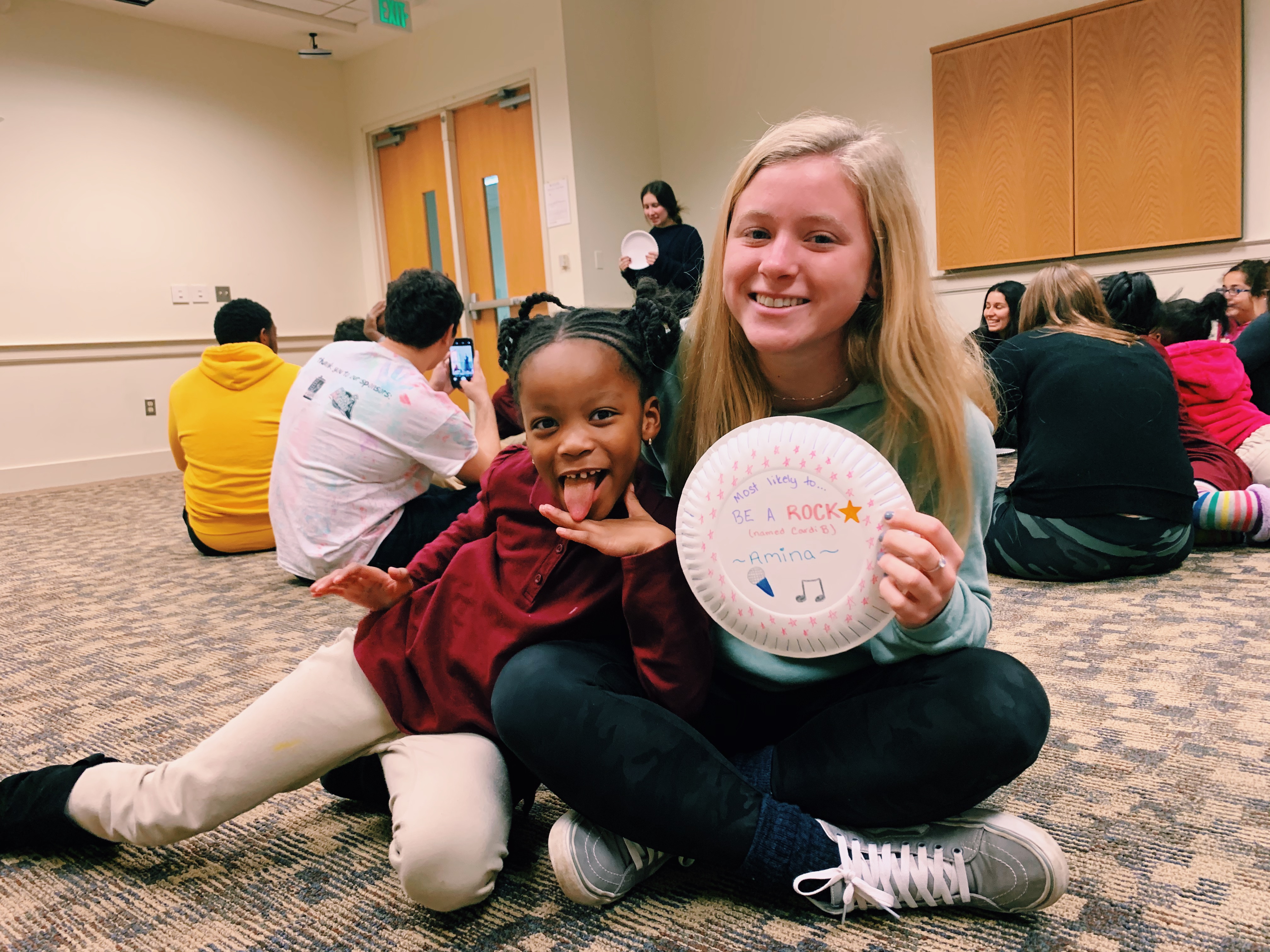 a photo of peyton and her "little buddy" sitting together on the floor, smiling