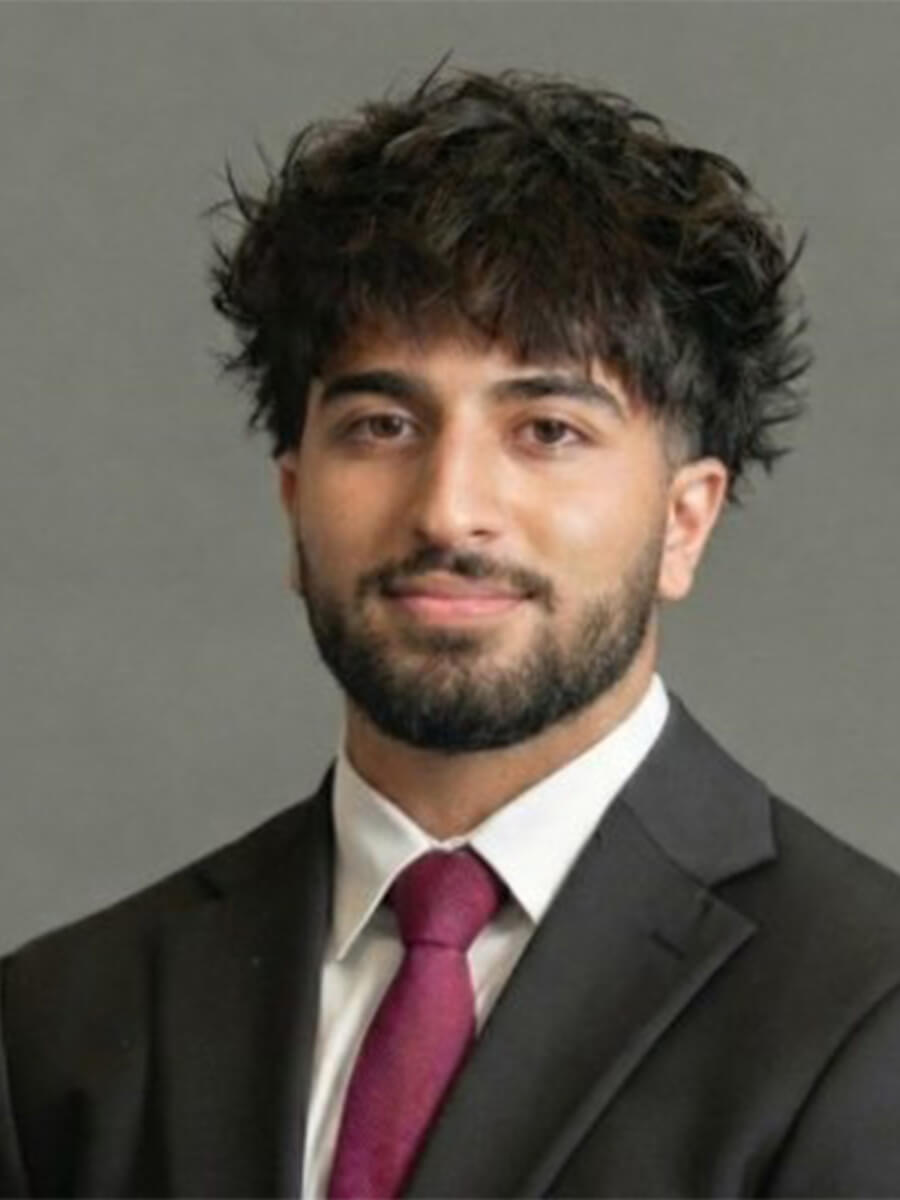 Shayaan's headshot is him slightly smiling in a black tux with a white shirt and red tye.