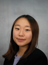 Emily Yi's headshot photo features her with in a black blazer with a gray background.