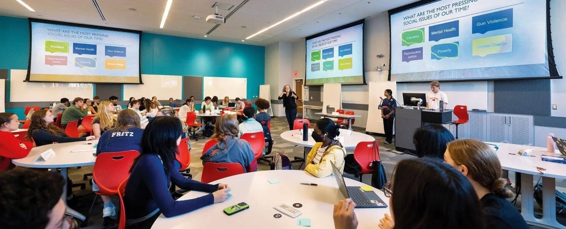 image of people sitting at round tables with large projection screens around the room.