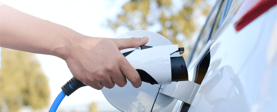 A hand moves to plug an electric vehicle charger into a white car.