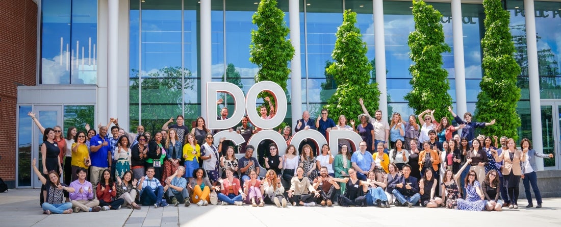 A large group of people gathered around the Do Good Sign with their hands in the air and smiling. 