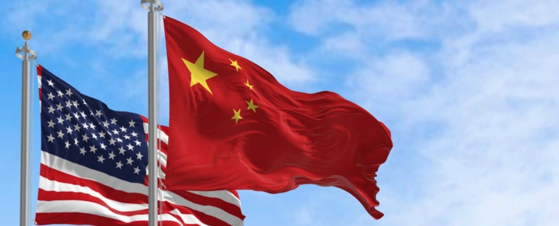 U.S. and China flags blowing in the wind on a bright, sunny day against a blue sky